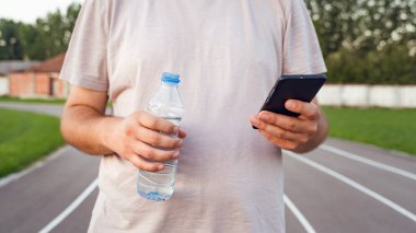 Koşu yolunda elinde cep telefonu ve bir şişe su tutan Kafkasyalı adamın orta kesimine yaklaş - Erkek, gün içinde ilerleme planlama ve izleme eğitimi için başvuru kullanıyor