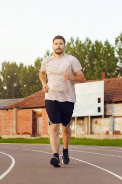 Hipodromda koşan yetişkin beyaz bir adamın ön manzara portresi - açık havada sakal eğitimi almış genç bir erkek - gerçek insanlar sağlık ve spor konsepti tam uzunlukta