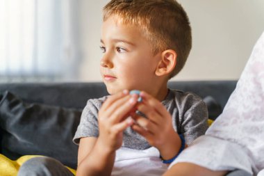 Evdeki kanepede oturan küçük beyaz çocuğun yakın plan portresi - küçük erkek çocuk yan tarafa bakıyor - yaz günü kanepede oynaşan çocuk - çocukluk aile hayatı kavramı