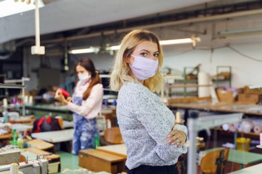 Genç beyaz kadın girişimci dikiş fabrikasında duruyor - kadın tasarımcı salgın sırasında koruyucu maske takıyor - Yeni normal kriz durgunluğu kavramı covid-19 iş dünyası