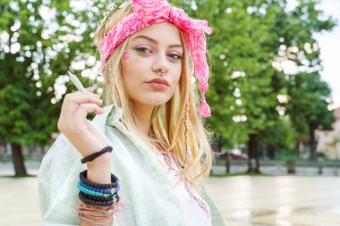 Sarışın, beyaz bir kadın elinde sigarayla dışarıda duruyor - güzel bir kız yaz gününde ortak sarma yapıyor - gençlik ve özgürlük konsepti şehir hayatı esrar yasallaştırma