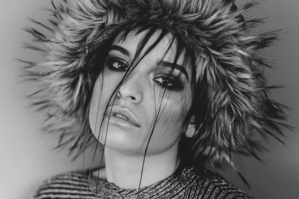 Portrait of young beautiful caucasian girl fashion woman female model with furry hat on her head and hair over face in day close up posing makeup black and white