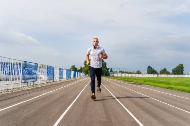 Koşu pistinde koşan yetişkin, beyaz bir adamın tam önü - yaz günü stadyum eğitiminde sarışın erkek atlet - gerçek insanlar sağlıklı yaşam tarzı konsepti