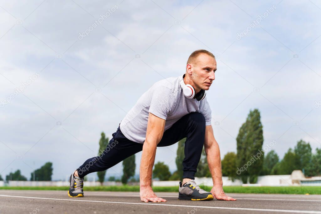 Low angle view on adult caucasian man stretching on the running track - Blonde male athlete preparing for training in summer day - real people healthy lifestyle concept