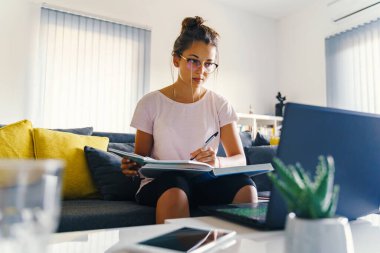 Evdeki dizüstü bilgisayarın önünde çalışan genç beyaz kadın hakkında ön görüş - Kız kitap okuyor ve notlar yazıyor sınav hazırlıyor online danışmanlık - eğitim ve öğrenim kavramı