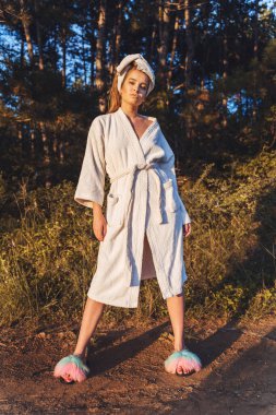 Front view full length of young beautiful caucasian woman standing on the dirt road in nature in sunny summer day wearing towel and bathrobe - Social norms equality confused generation concept clipart
