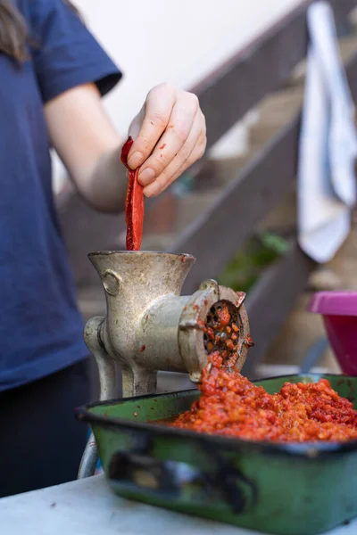 Close up outdoor on female hand on grinder mill for vegetables preparing paprika baked red pepper for ajvar national dish in balkan - healthy organic food concept