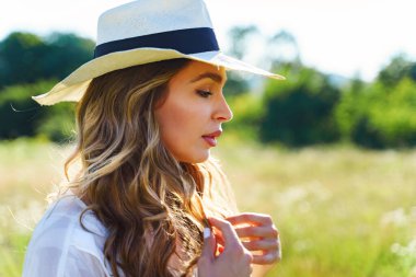 Yan görünüş, yaz günü tarlada şapkalı güzel beyaz kadın portresi. Kapalı hayaller kuruyor.