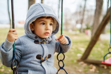 Kışlık paltolu küçük beyaz bir çocuğun sonbahar günü parkta sallanışı - büyüyen konsept içinde büyüyen boş zaman aktivitesinin kopyası