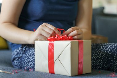 Bilinmeyen Kafkas kadın orta kesimini kapatın ve elleri kırmızı kravat kurdelesiyle paketlenmiş kutunun üzerinde kanepede otururken veya açılırken - doğum günü hediyesi veya bayram hediyesi vermek ve almak kavramı