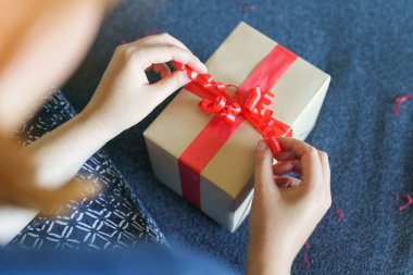 Bilinmeyen beyaz kadın göbeğini kapatın ve elleri kanepede oturmuş kırmızı kravat kurdeleli kutuyu hazırlıyor. Doğum günü hediyesi ya da bayram hediyesi.