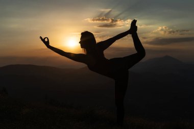 Kadın silueti, gün batımına karşı dağın tepesinde yoga yapıyor meditasyon esneme ve rahatlama kavramına karşı.