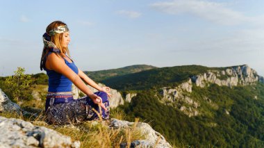 Yazın ya da sonbaharda Lotus Yoga pozisyonunda dağın tepesinde oturan Kafkasyalı kadının yan görüntüsü - Meditasyon ve rahatlama maneviyatı konsepti boşluk kopyalanması