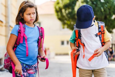 Küçük beyaz erkek ve kız kardeşlerin ön manzara portresi ya da küçük arkadaşlar okula giden birinci sınıf öğrencileri güneşli bir günde sırtlarında sırt çantalarıyla geziyorlar.