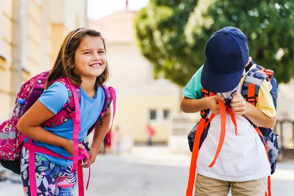 Küçük beyaz erkek ve kız kardeşlerin ön manzara portresi ya da küçük arkadaşlar okula giden birinci sınıf öğrencileri güneşli bir günde sırtlarında sırt çantalarıyla geziyorlar.