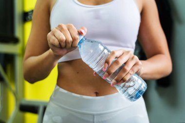 Kafkasyalı bir kadın ya da kadının spor salonunda elinde bir şişe su tutup açtığı orta bölüme yaklaşın. Hidrasyon konseptini gündüz çalıştıran sportif bir kadın.