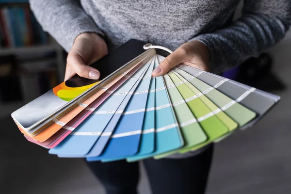 Close up on hands of unknown female person holding color palette at home in apartment - Woman choosing paint material for house renovation - decoration and innovation concept