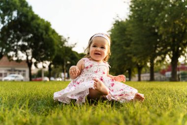 Küçük beyaz bir kız çocuğu çimlerin üzerinde oturuyor yaz ya da sonbahar günü tarlada elbise giyiyor mutlu bir şekilde gülüyor çocukluk konsepti