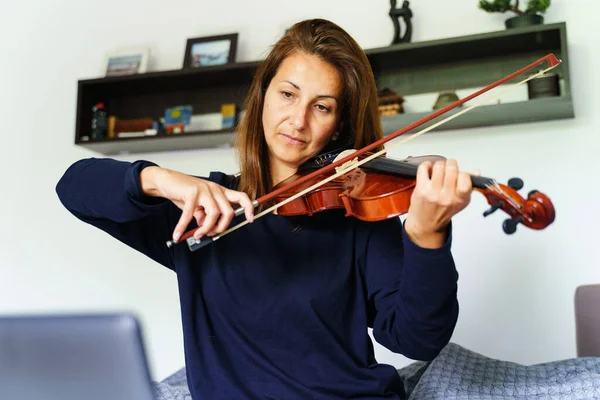 家庭での大人の白人女性の正面図寝室で彼女のベッドの中に座ってオンライン指導ビデオクラスを見ながらバイオリンを再生する方法を学ぶ リアル人々レジャーコンセプト — ストック写真