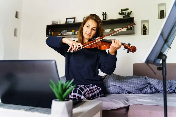 家庭での大人の白人女性の正面図寝室で彼女のベッドの中に座ってオンライン指導ビデオクラスを見ながらバイオリンを再生する方法を学ぶ リアル人々レジャーコンセプト — ストック写真