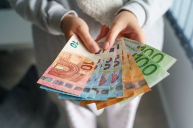 Avro banknotları maaş artışlarını sayarken ya da faturaları ödemeye hazırlanırken elinde bir yığın para tutan ve sayan Kafkasyalı kadının ellerini kapatın.