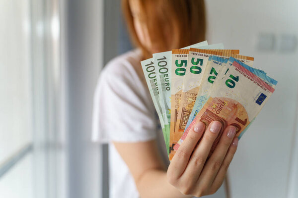 Close up on hands of unknown caucasian woman holding a pile of money EURO EUR banknotes counting salary receiving raise or preparing to pay bills