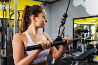 Genç beyaz kadın spor salonunda makineyle antrenman yaparken yan görünüm - kopyalama alanı