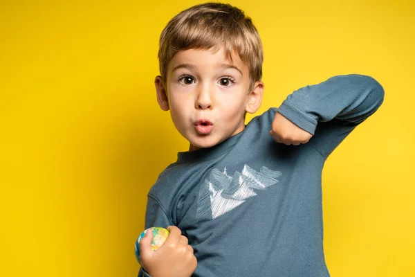 Portrait of happy joyful small caucasian boy in front of yellow background making faces - Childhood growing up and achievement concept - front view waist up copy space