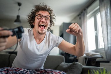 Yetişkin erkek, beyaz erkek, evde oyun konsolu video oyunu oynuyor. Oyun kumandası sizde. Keyfinize bakın ve kazanın ve başarı konseptini kopyalayın.