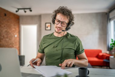 Kafkasyalı bir erkek, evinde kulaklıkla bilgisayar başında müşteri destek, güler yüzlü, güler yüzlü.