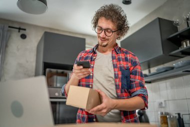 Beyaz bir adam online alışveriş ürünlerinin nakliye detaylarını kontrol etmek için akıllı telefon kullanıyor. Akıllı telefon uygulaması başvurusunu kontrol edin. Çevrimiçi detaylar mutlu bir gülümseme.