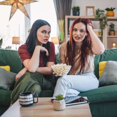 Kafkasyalı iki genç kız ya da erkek kardeş evde televizyon dizisi izleyip patlamış mısırla kanepede oturuyorlar.