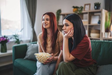 Kafkasyalı iki genç kız ya da erkek kardeş evde televizyon dizisi izleyip patlamış mısırla kanepede oturuyorlar.