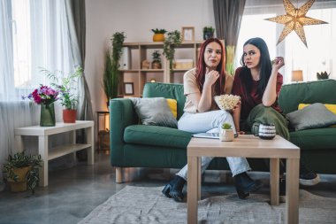 Kafkasyalı iki genç kız ya da erkek kardeş evde televizyon dizisi izleyip patlamış mısırla kanepede oturuyorlar.