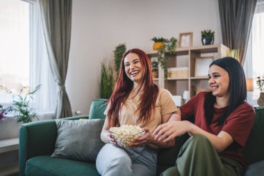 Kafkasyalı iki genç kız ya da erkek kardeş evde televizyon dizisi izleyip patlamış mısırla kanepede oturuyorlar.
