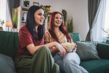 Kafkasyalı iki genç kız ya da erkek kardeş evde televizyon dizisi izleyip patlamış mısırla kanepede oturuyorlar.
