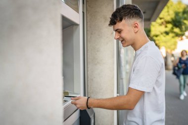 Genç bir erkek öğrenci kredi kartı kullanıyor ve ATM 'den para çekiyor.
