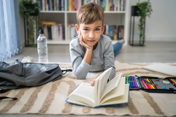 caucasian boy pupil student read book at home on the floor study learn prepare for school