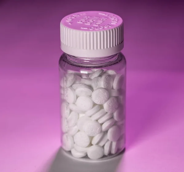 Frasco de pastillas de aspirina blanca sobre un fondo rosa — Foto de Stock