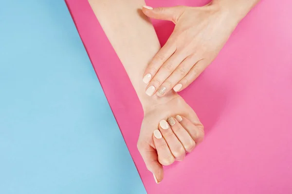 Woman hands with nails manicure on blue and pink background. Manicure and Beauty hand concept. Close up, top view