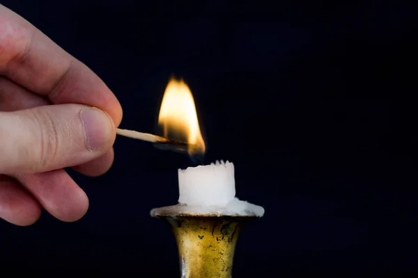 Man hand with Matchstick light flame on candle in candlestick, close up