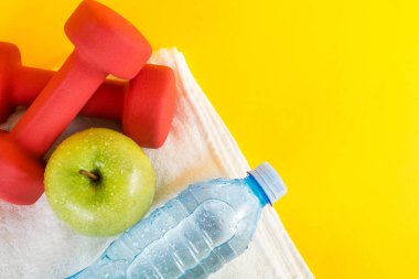 Beyaz havlu ve sarı alan üstten görünüm kırmızı dambıl, yeşil elma ve çiy ile taze su şişesi. Diyet, spor, fitness ve sağlık gıda ve içecek konsepti