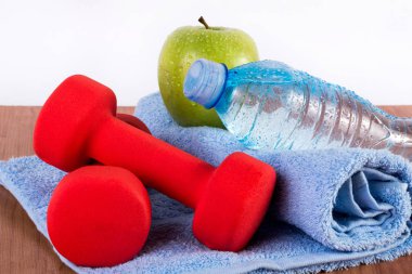 Kırmızı halter, taze su şişesi ile mavi havlu üzerinde çiy ve yeşil elma. Fitness, spor ve sağlıklı gıda kavramı