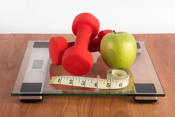 Weight scale with red dumbbell, measuring tape and fresh green apple on wooden floor. Diet, sport, fitness and recreation concept — Stock Image Weight Scale Red Dumbbell Measuring Tape Fresh Green Apple Wooden Royalty Free Stock Images