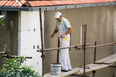 Nis, Sırbistan - 16 Haziran 2018: Çalışan beyaz üniforma iskele üzerinde adam. Sıvacı yeni cephe duvar ev yalıtır