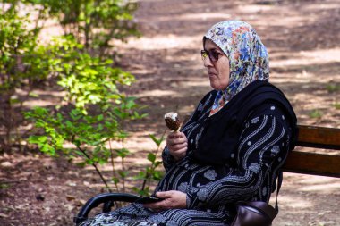 Niska Banja, Sırbistan - 02 Temmuz 2018: Müslüman yaşlı kadın tezgah rahatlatıcı ve Doğa Parkı gölgede yiyor buz tıkmak. Tatil ve yaz kavramı keyfi