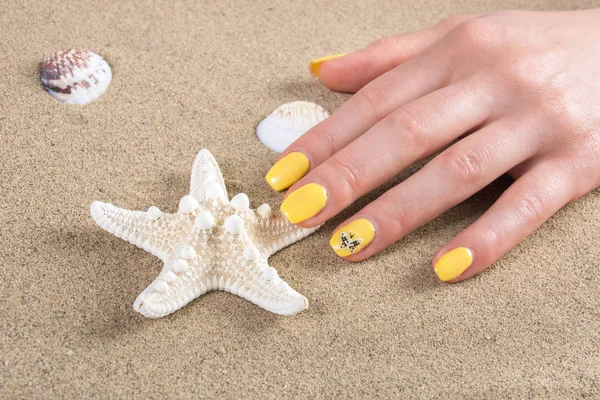 Woman with yellow nails manicure polish touching starfish on sea sand on beach. Close up, selective focus