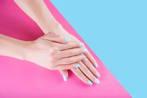 Young female hand with blue manicure nails polish on pastel pink and blue background. Femininity and beauty concept. Close up, selective focus