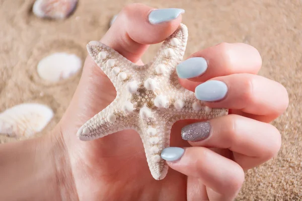 Jente Med Blå Manikyrnegler Holdt Sjøstjerne Hånden Sandstrand Bakgrunnen Sommerferie – stockfoto