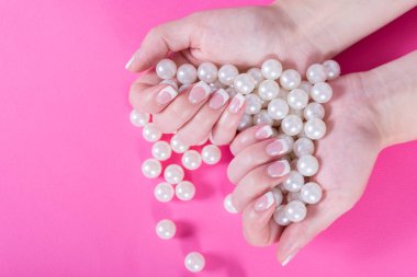 Genç kadın birçok inci el ile tutarak, pembe arka plan izole çivi Lehçe Fransızca. Manikür ve kadınlık kavramı. Yakın, seçici odak